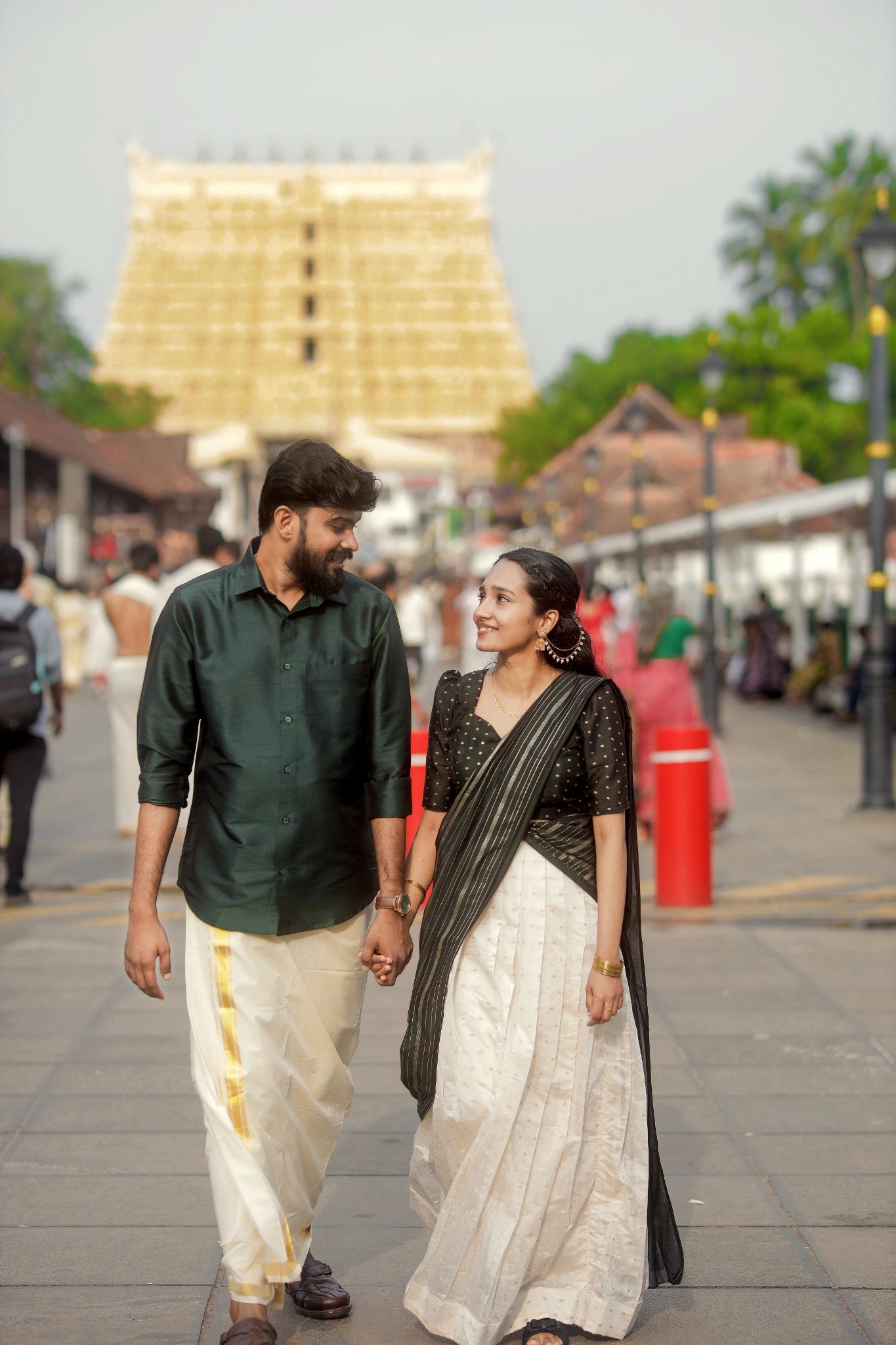 Abhinand and Akshaya walking hand in hand in traditional Kerala attire in front of a temple gopuram