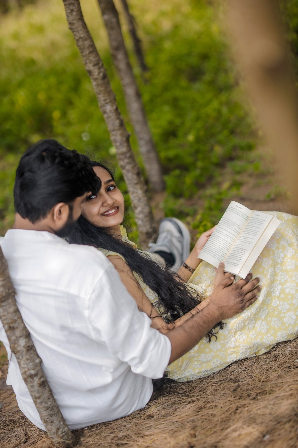 The couple sitting under trees reading a book together